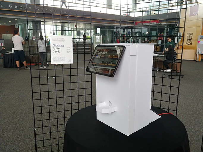 The installation on a table inside a mesh display booth, with a sign reading Click Here To Get Candy.